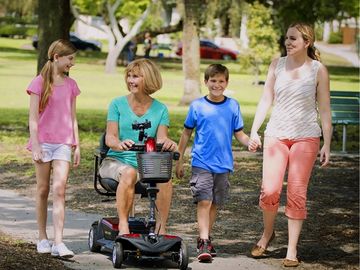 Woman using mobility scooter through park with three other people walking nearby