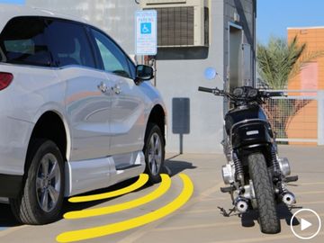 Wheelchair accessible van parked in disability parking spot. Motorcycle parked in ramp access space.