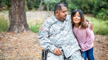 Child standing next to man in a military uniform and seated in a wheelchair