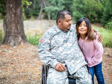 Child and wheelchair user in military uniform embracing