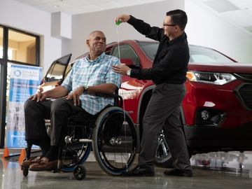 Person measuring height of man seated in a wheelchair in the showroom of a wheelchair accessible van dealership