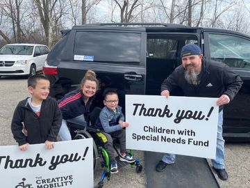 Family beside a wheelchair accessible van with the ramp deployed and holding signs that read "Thank You The Creative Mobility Group" and "Thank You Children with Special Needs Fund"