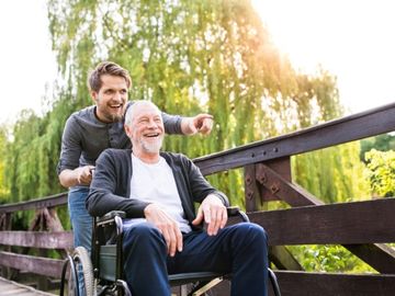 Younger man assisting an older man in a wheelchair on a bridge