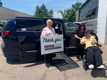 3 people beside a wheelchair accessible minivan with the ramp deployed holding a sign that reads, "Thank you Michigan Rehabilitation Services."