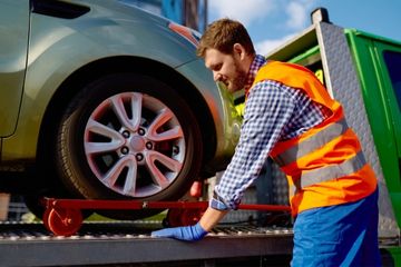 Man in reflective vest securing a wheelchair van onto a tow truck