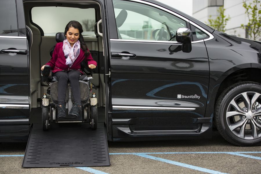 Woman using a power wheelchair and exiting a wheelchair accessible Chrysler Pacifica van.