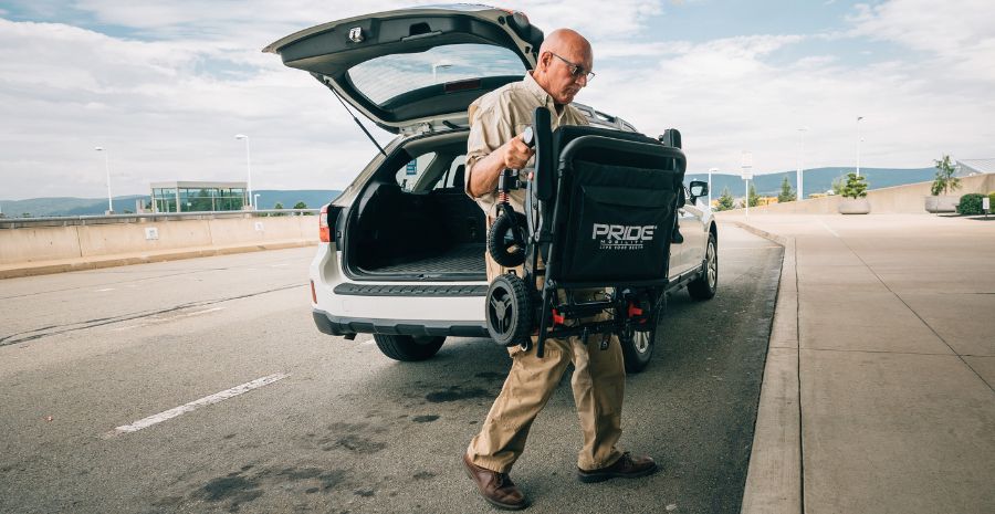 Man unloads folded power wheelchair from trunk of vehicle