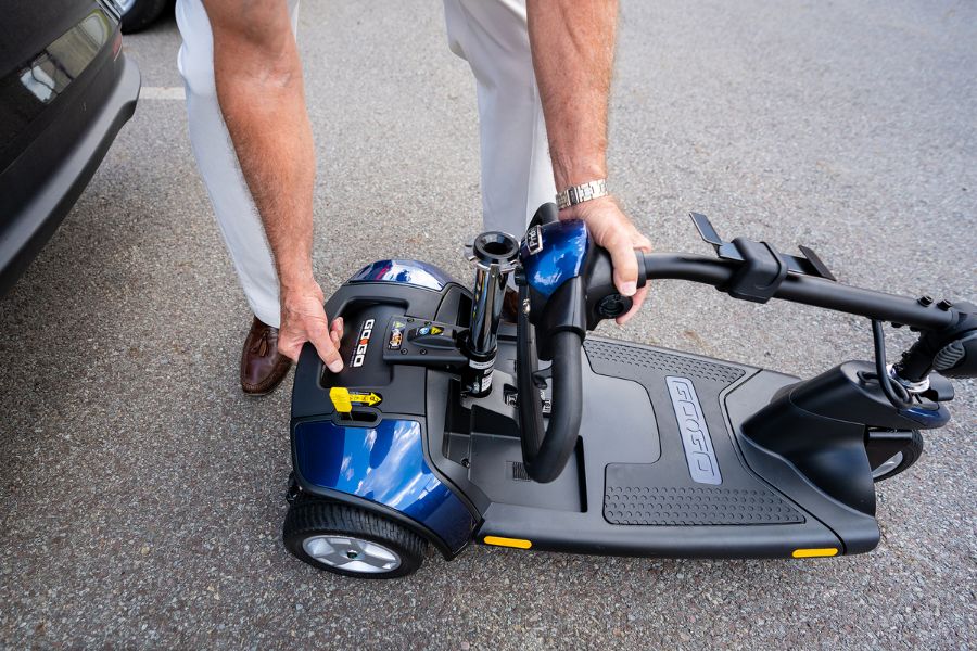 Man preparing to lift a disassembled mobility scooter into the trunk of a sedan
