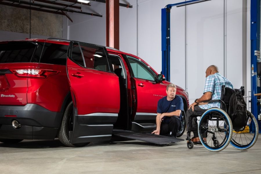 Technicians kneeling beside deployed ramp of wheelchair accessible SUV while speaking with customer