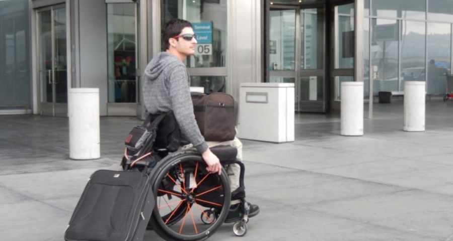 Wheelchair user waiting outside of airport with baggage