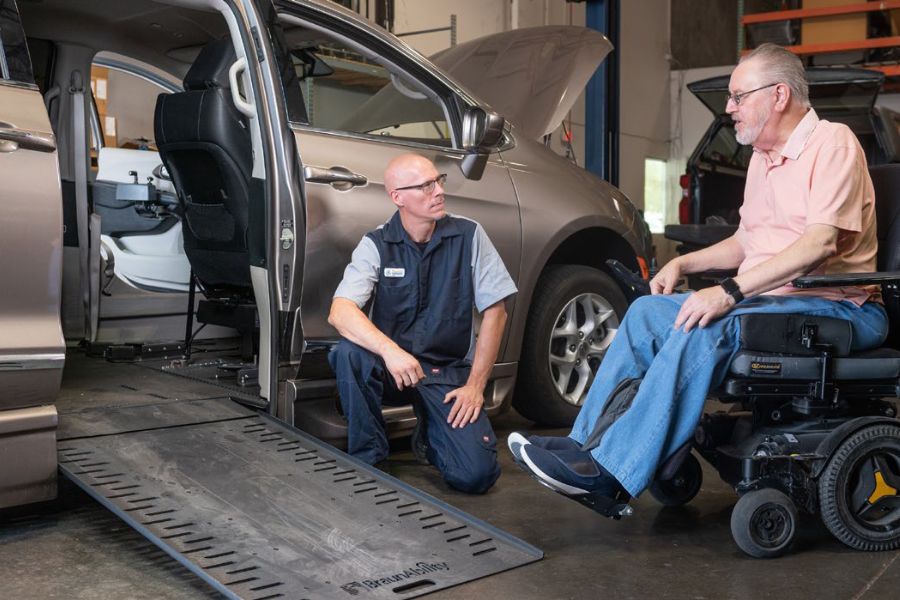 Wheelchair accessible van in repair shop. A service technician and a person using a wheelchair are talking beside the van.