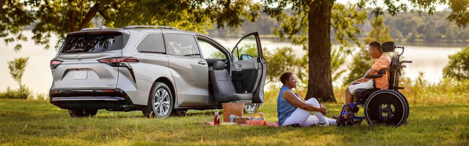Mother and son enjoying a picnic in the park. Son, in a wheelchair, sits beside his mother on a picnic blanket. A BraunAbility Turny Evo seat is rotated out of their van, parked in the background with the front-passenger door ajar.