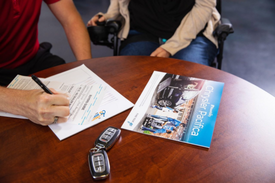 Customer signing paperwork for wheelchair accessible vehicle financing during a consultation with a mobility specialist