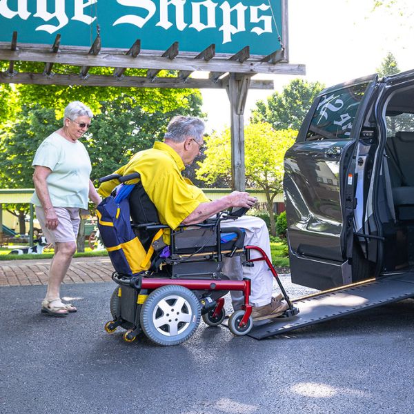 Senior using a power wheelchair entering a wheelchair accessible van with ramp while spouse walks nearby
