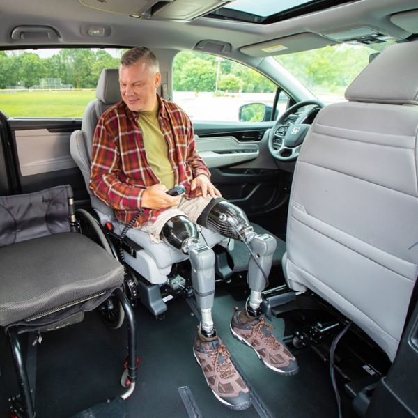 Person with prosthetic legs transferring from wheelchair into a wheelchair accessible vehicle, emphasizing independent mobility