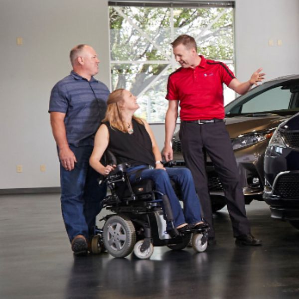 Mobility specialist discussing wheelchair accessible van options with a client using a power wheelchair in a showroom